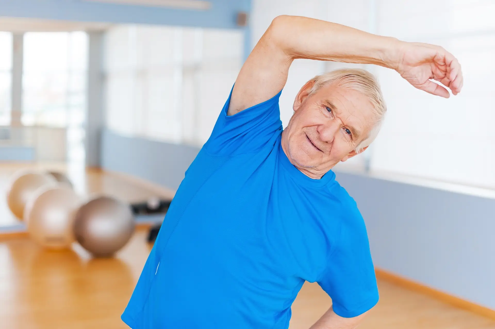 Active senior man. Cheerful senior man doing stretching exercises and smiling while standing indoors