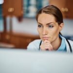 Pensive doctor working on her desktop PC at doctor's office.