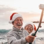Portrait of two cute old persons having fun and enjoying together at the beach on christmas days