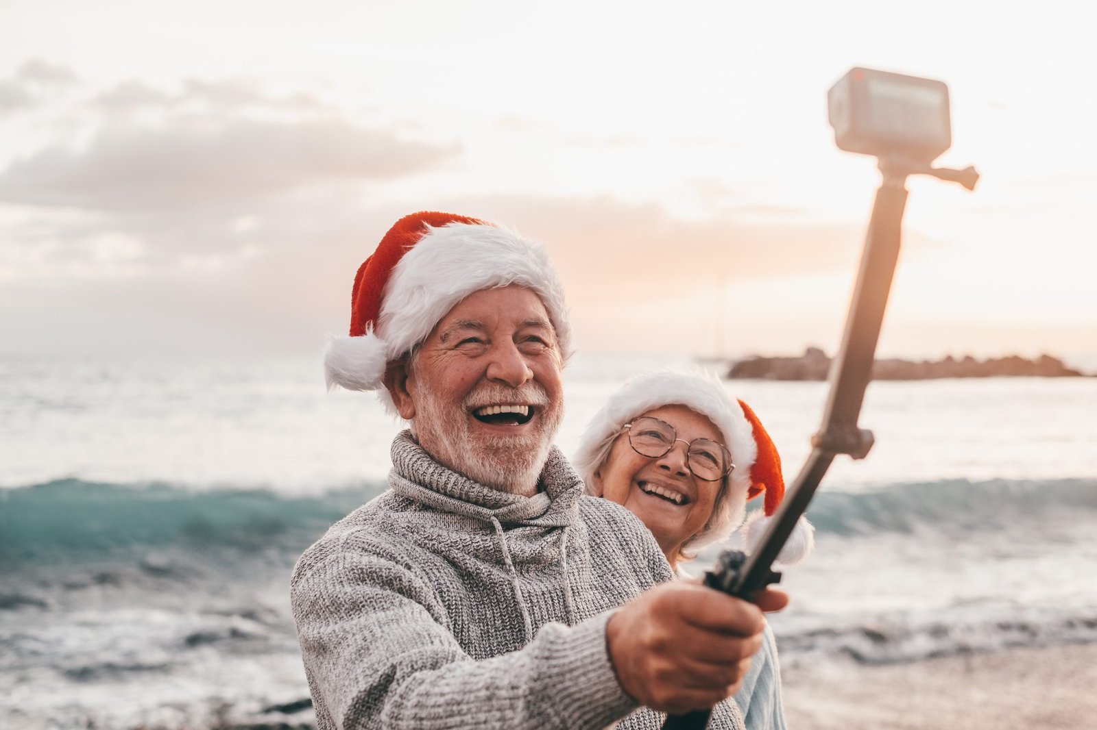 Portrait of two cute old persons having fun and enjoying together at the beach on christmas days