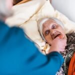 Woman taking care of old woman lying in bed