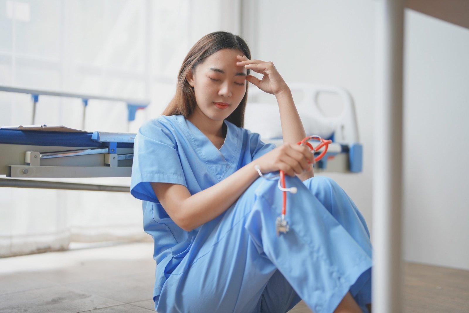 Young doctor experiencing burnout sitting on hospital floor