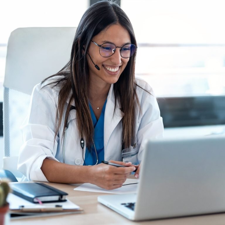 Female doctor talking with colleagues through a video call with a laptop in the consultation.