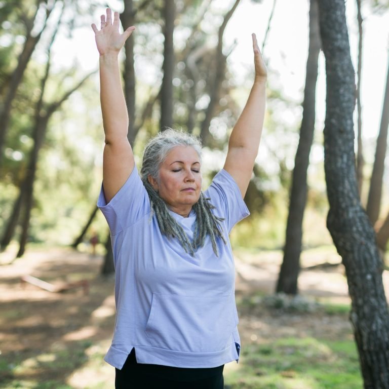 Mature old woman with dreadlocks practicing yoga and tai chi outdoors - wellbeing and wellness