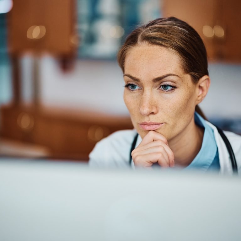 Pensive doctor working on her desktop PC at doctor's office.