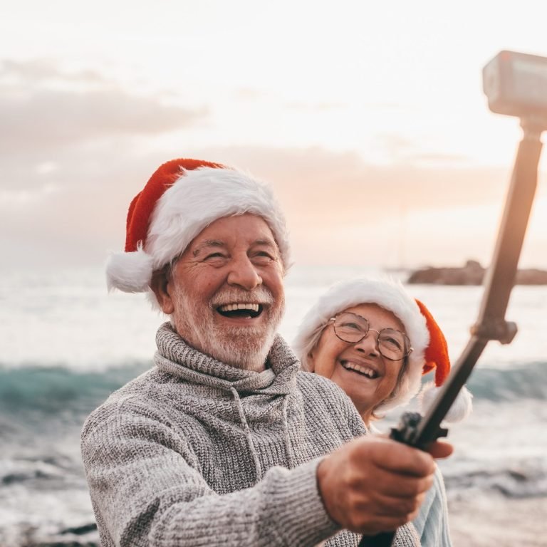 Portrait of two cute old persons having fun and enjoying together at the beach on christmas days