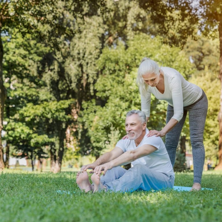 Senior woman helping to stretch mature man outdoors at park while doing workout and yoga exercices